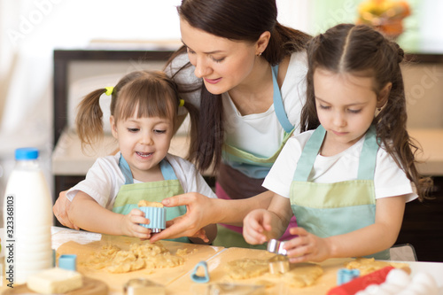 Mother and kids daughters weared aprons making cookies together