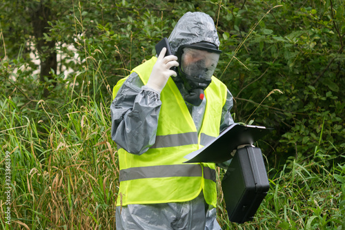 a specialist in a protective suit reports on the phone according to the results of an environmental study looking at the data recorded on a paper tablet
