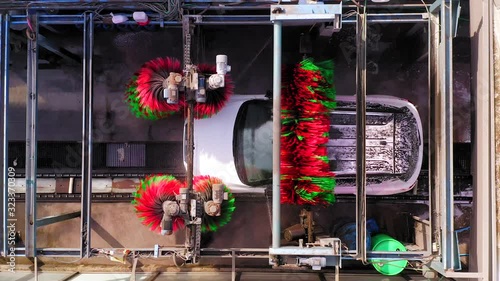 Car wash tunnel with single Car, brushes spinning and water sprinklers, Top down aerial view.