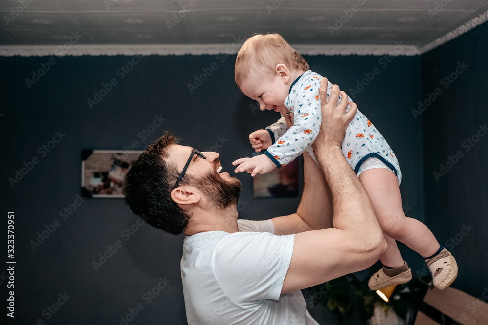 Fototapeta premium Father and son. Father throws the baby up in the air and smiles at him. Love dad and baby. Father and son look at each other. Son examines and hugs dad's face.