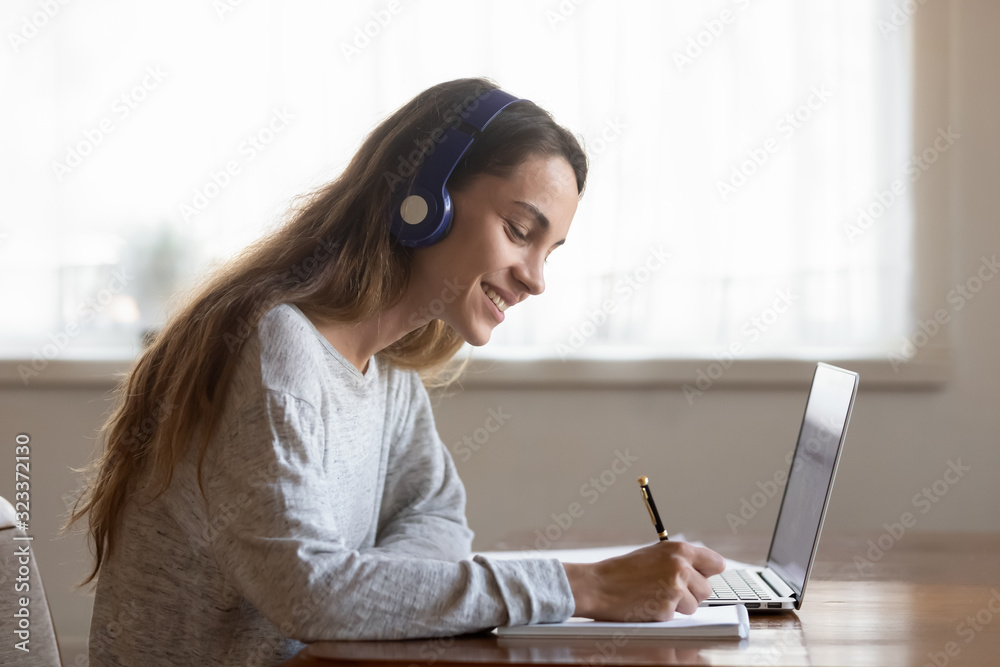 Smiling young woman in earphones studying on laptop Smiling young woman in earphones studying on laptop