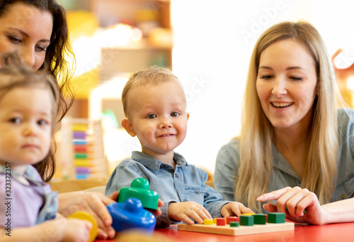 Baby girl and toddler boy with moms play with color wooden puzzle in a montessori classroom