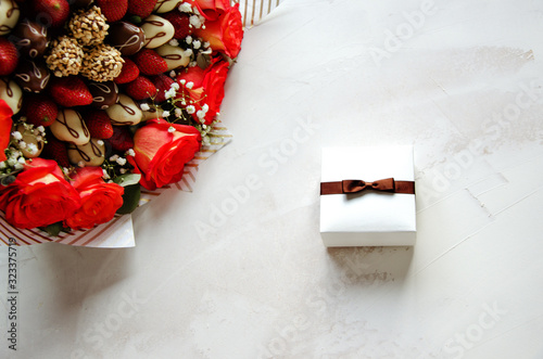 Composition of red-yellow pink flowers, fresh strawberries and fresh strawberries in chocolate on a white background. In the center of the composition, the gift box is tied with a bow. Mother's day