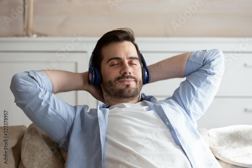 Calm young man listen to music relaxing on couch