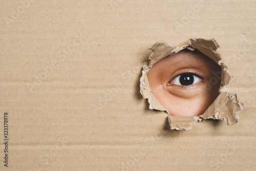 Принти на полотні Boy eye peeking through a hole on a cardboard box with shocking gesture