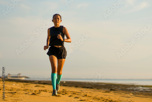 outdoors fitness portrait of young attractive and athletic Asian Indonesian woman in compression socks jogging on the beach doing running workout training hard