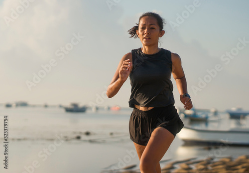 outdoors fitness portrait of young attractive and athletic Asian Indonesian woman in her 40s running on the beach doing intervals workout in athlete training concept