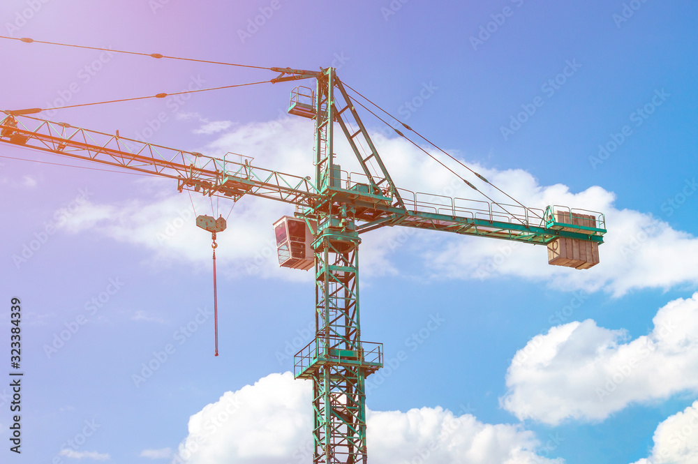 Tower crane on a background of blue sky with clouds, colorful light of the sun Tower crane on a background of blue sky with clouds, colorful light of the sun