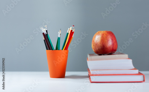 Orange pencil holder, stack of books on white table with red apple. Books stacking. Back to school concept. Copy Space. Education learning background. © Inna