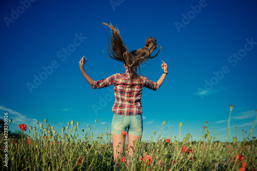 Beautiful girl in poppy field. Young girl with long hair among the blossoming poppy field.