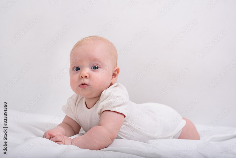 Portrait of a cute 3 months baby lying on bed. Baby lying on stomach on white sheets Portrait of a cute 3 months baby lying on bed. Baby lying on stomach on white sheets