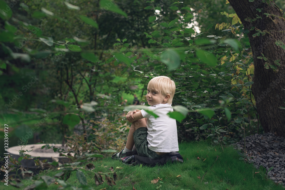Little blond boy sitting on grass in the Park. Independent child Little blond boy sitting on grass in the Park. Independent child