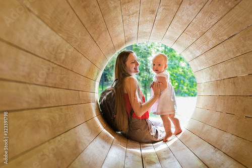 Mother and baby playing on the Playground in the wooden tunnel. Eco-friendly natural playground photo