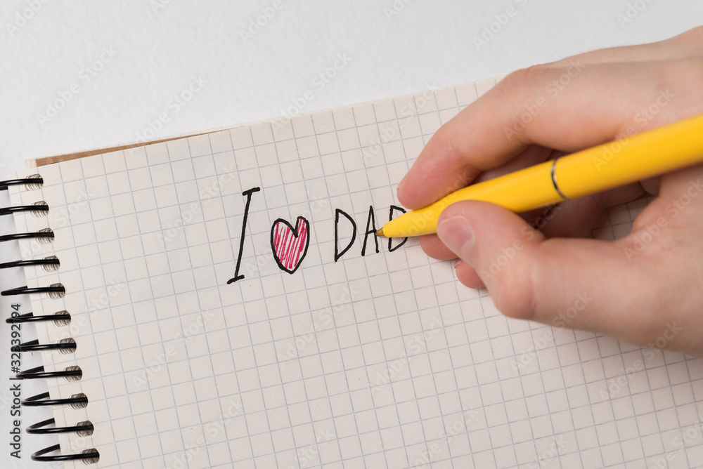 Children's hand writes the words I love dad. Notebook on white background. Father's day. Children's hand writes the words I love dad. Notebook on white background. Father's day.