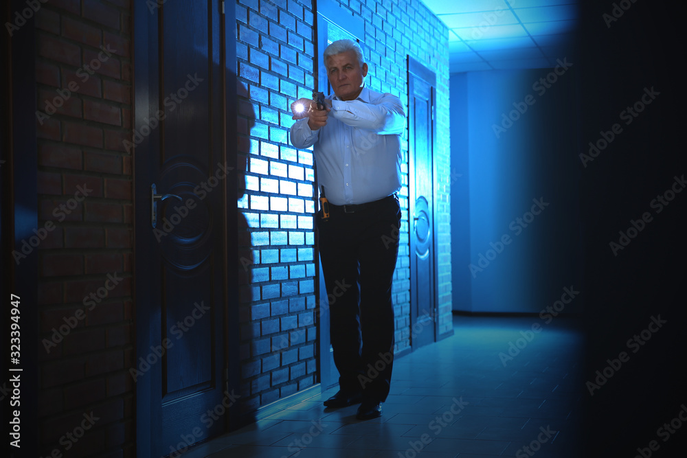 Professional security guard with gun and flashlight checking dark hallway