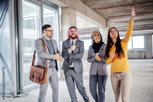 Canvas Print Two arab foreign investors standing in building in construction process and listening to real estate agent who is trying to convince them to buy it