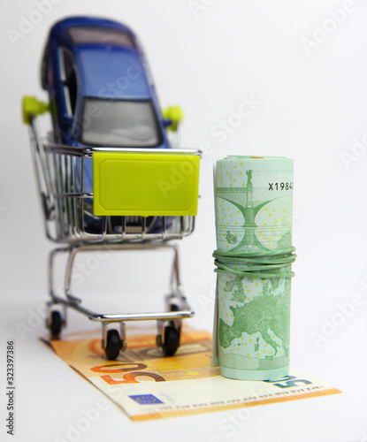 Car purchase.  Euro banknotes,  toy blue car and shopping trolley . White background. photo