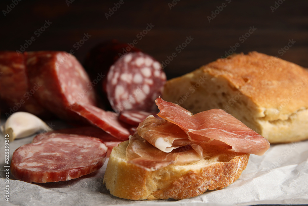 Delicious bread with prosciutto and other sausages on parchment paper, closeup