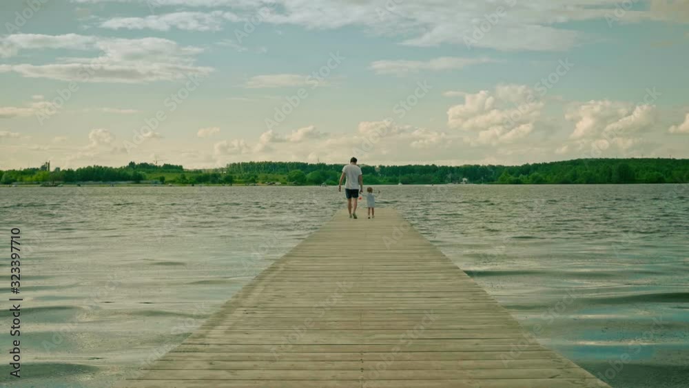 dad and little girl walk joining hands on river wooden pier dad and little girl walk joining hands on river wooden pier