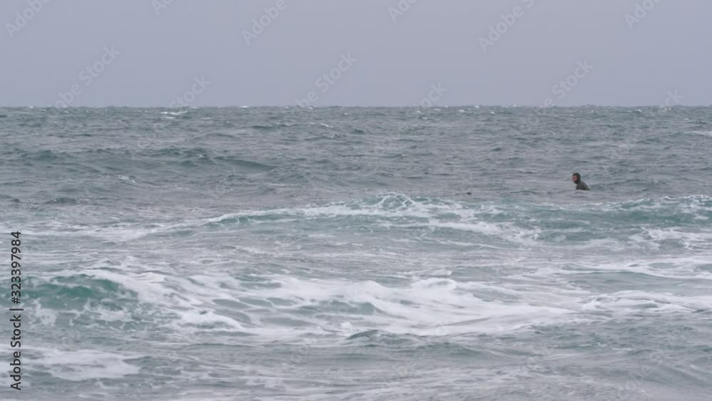 Two surfers in wetsuits try to catch a wave in a severe storm in the Pacific ocean in winter Two surfers in wetsuits try to catch a wave in a severe storm in the Pacific ocean in winter