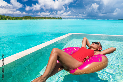 Summer swimming pool woman relaxing on donut float enjoying luxury resort vacation sunbathing fun. Red swimsuit suntan girl happy.