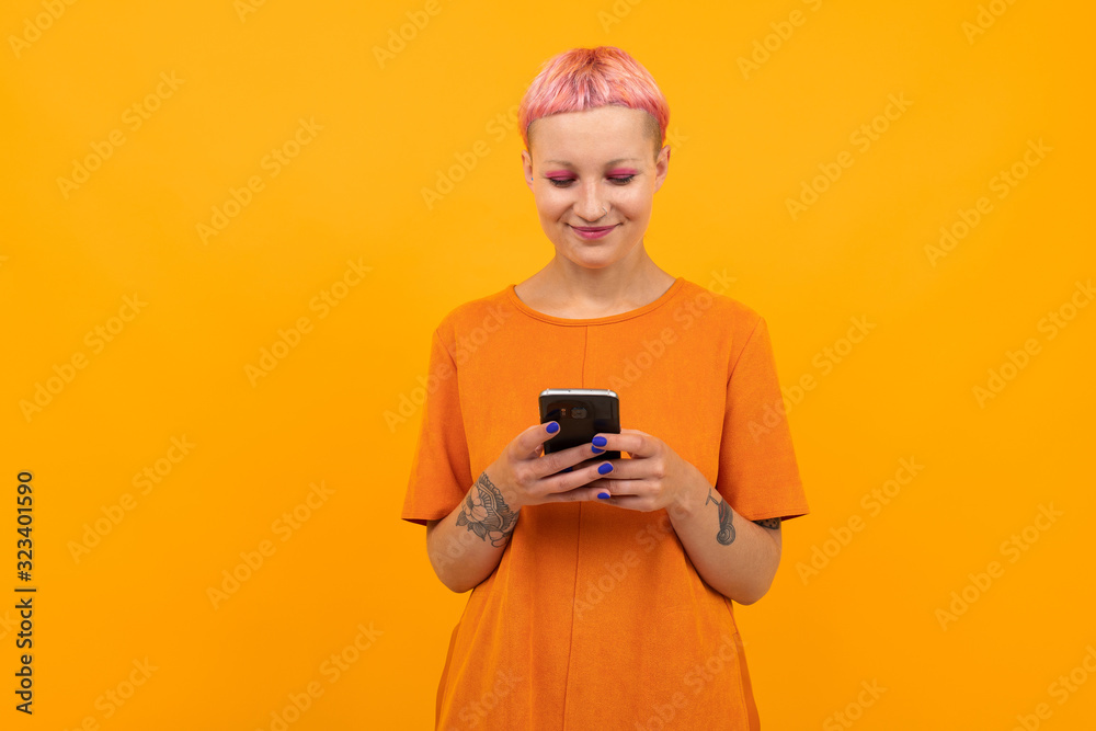 Fototapeta premium Extraordinary beautiful woman with short pink hair and big tattoo on her hand smiles isolated on orange background