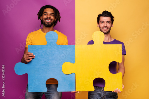 Friends with puzzles in hand over yellow background. Concept of integration, union and partnership photo