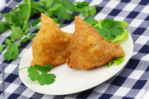 Two Indian samosas on green lettuce on white plate and fresh coriander leaves