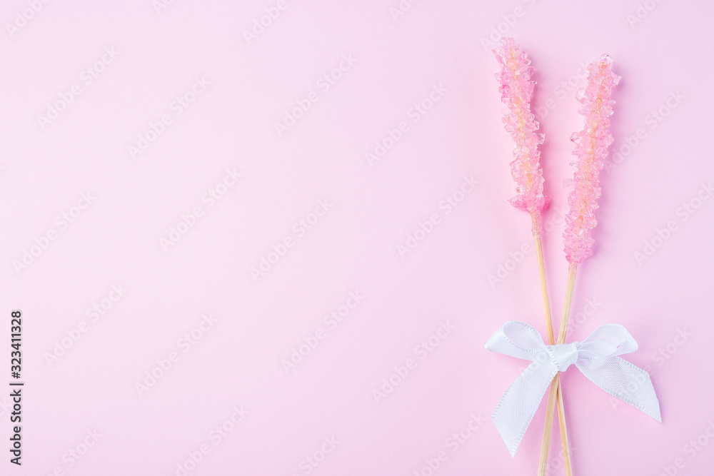 Two pink rock candy on pink paper background decorated with a white bow, copy space, horizontal, top view