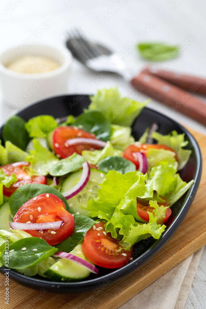 Healthy vegetable salad from fresh vegetables of tomato, spinach, cucumber, lettuce and sesame on a plate. Useful nutrition.