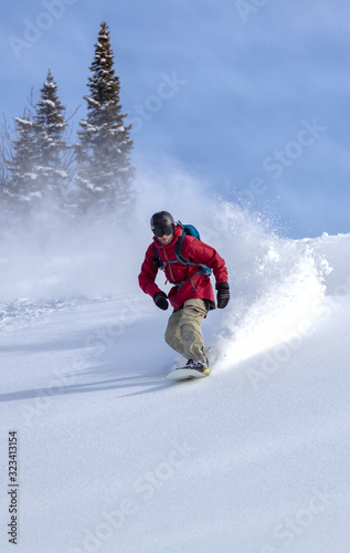 heliski snowboarding. freerider in a bright suit rides snowboarding with large splashes of snow on a sunny day. Young snowboarder. concept snowboard. big swirls of fresh snow in Good powder day