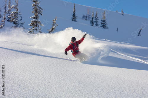 heliski snowboarding. freerider in a bright suit rides snowboarding with large splashes of snow on a sunny day. Young snowboarder. concept snowboard. big swirls of fresh snow in Good powder day