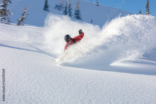 heliski snowboarding. freerider in a bright suit rides snowboarding with large splashes of snow on a sunny day. Young snowboarder. concept snowboard. big swirls of fresh snow in Good powder day