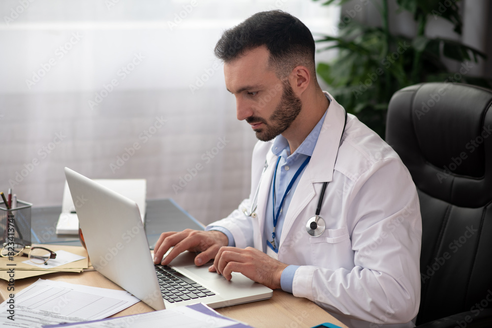 Young bearded doctor in a white robe looking busy Young bearded doctor in a white robe looking busy
