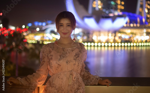 Asian Chinese girl in happy mood smiling for the camera in urban city background which is fully lighted up at night in Singapore