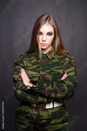 A girl soldier in camouflage clothing poses in a Studio