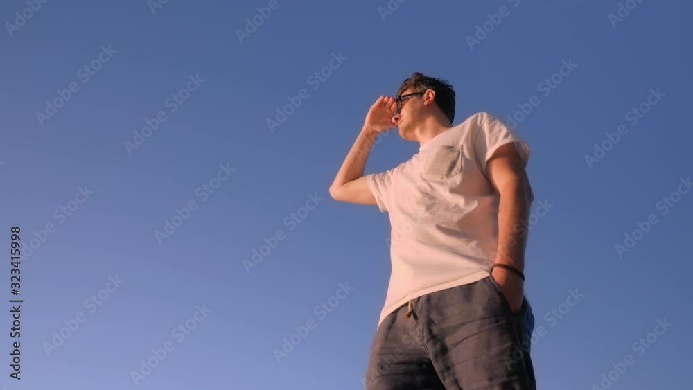 young man in trendy sunglasses and casual clothes under sky young man in trendy sunglasses and casual clothes under sky