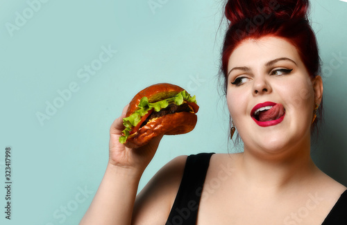 Happy size-plus overweight fat woman happy hold burger cheeseburger barbeque sandwich with beef  on pastel turquoise