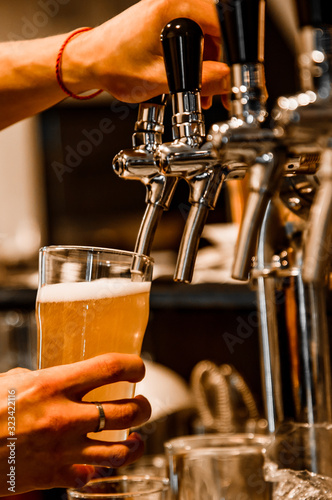 bartender hand at beer tap pouring a draught beer in glass serving in a restaura Fototapeta