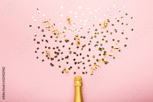 Bottle of champagne and confetti on pink background