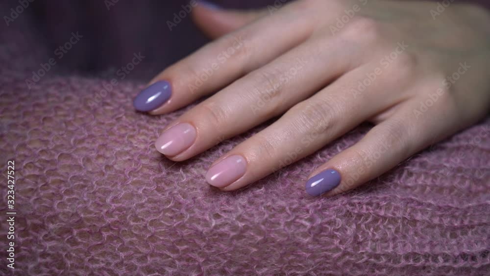 Closeup view of one female hand with pastel purple and pink manicured nails isolated on knitted violet sweater texture. Closeup view of one female hand with pastel purple and pink manicured nails isolated on knitted violet sweater texture.