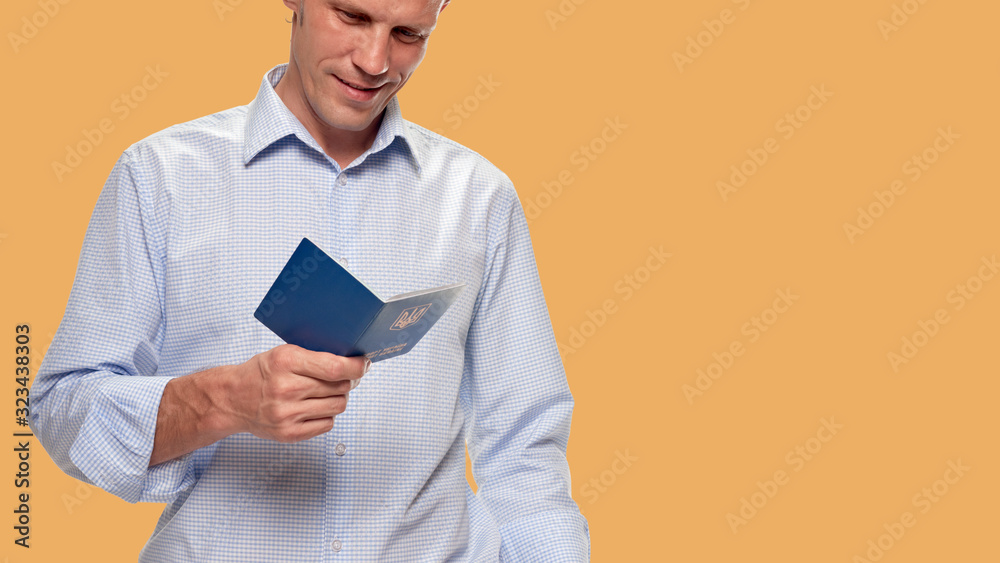 young man tourist holding passport and traveling with visa-free regime on orange skin color background young man tourist holding passport and traveling with visa-free regime on orange skin color background