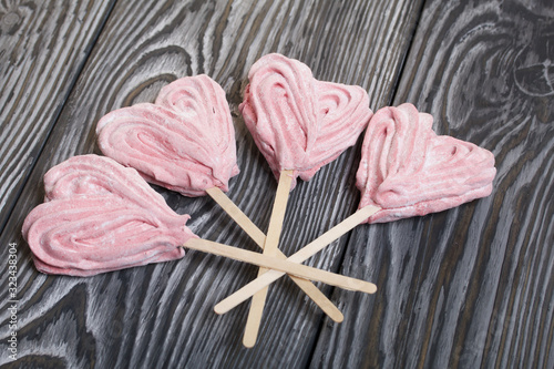 Delicate pink marshmallows in the shape of a heart on a stick. Several pieces are fan-shaped on brushed pine boards painted black and white.
