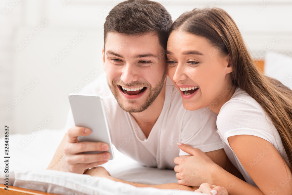Excited Couple Using Cellphone Texting Lying In Bed At Home Excited Couple Using Cellphone Texting Lying In Bed At Home