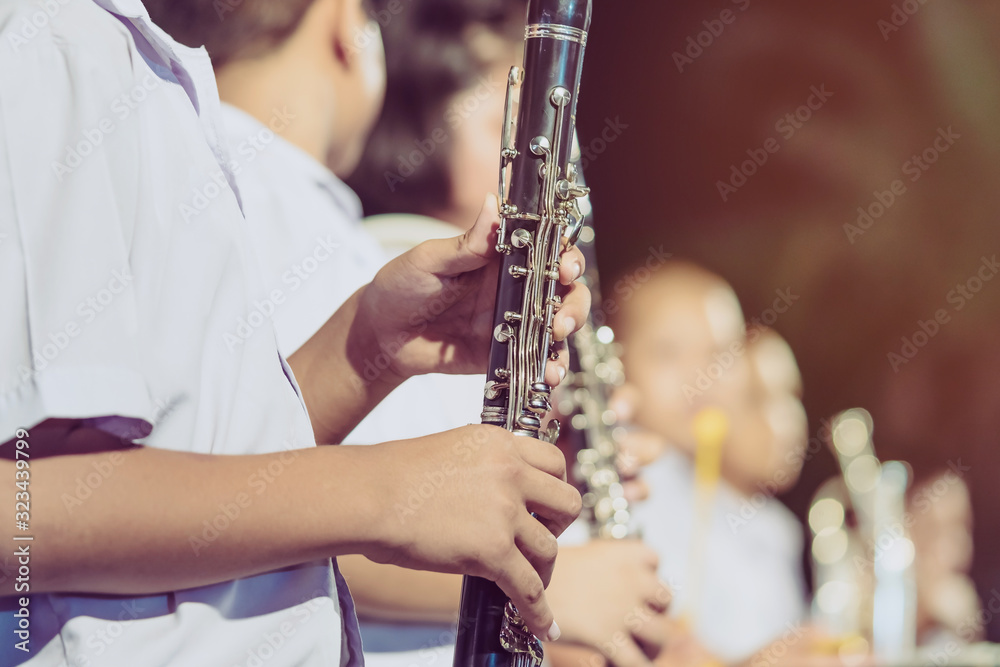 Fototapeta premium Male student with friends blow the clarinet with the band for performance on stage at night.