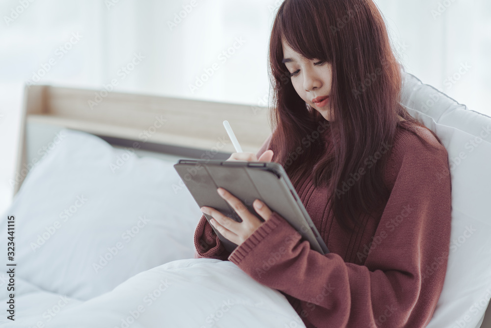A woman playing a tablet on the bed in a white bedroom A woman playing a tablet on the bed in a white bedroom