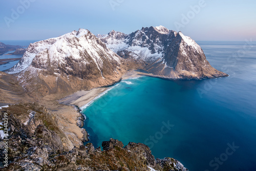 Landscape shot from Ryten towards Kvalvika beach in Lofoten island in Norway during blue hour. Snow cover the peaks in the background.