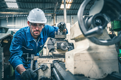 Male worker in blue jumpsuit and white hardhat operating lathe machine.  photo