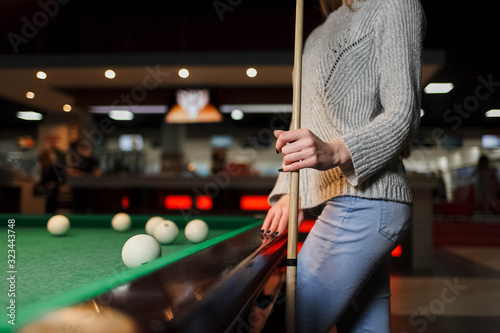 girl with a cue in hands stands near a billiard table