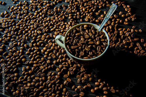 a cup of coffee beans stands on a black wooden table, coffee beans are scattered around.